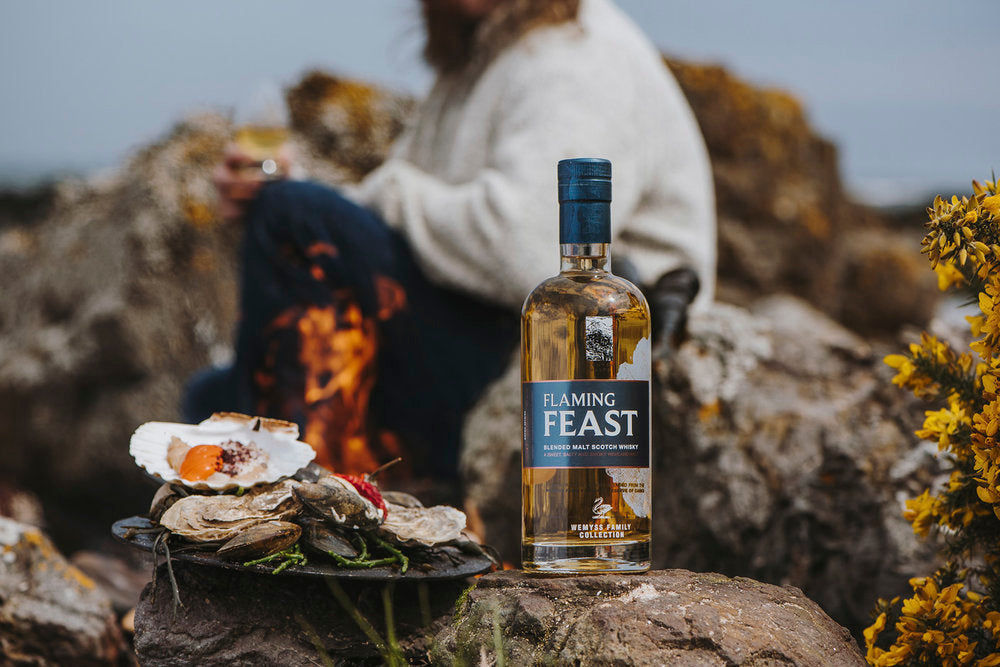 Flaming Feast bottle photographed on a rock alongside a plate of oysters